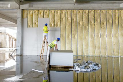 Riggers are working on thermal partition dry wall with mineral w Workers are assembly gypsum wall. Plasterboard is under construction using wooden ladder.